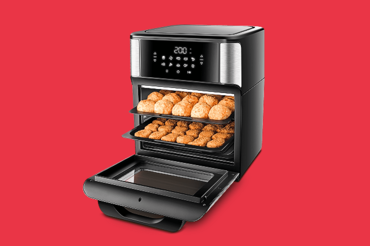 Mão posicionando uma forma de silicone vermelha com furos dentro do cesto aberto de uma fritadeira air fryer sobre uma bancada limpa